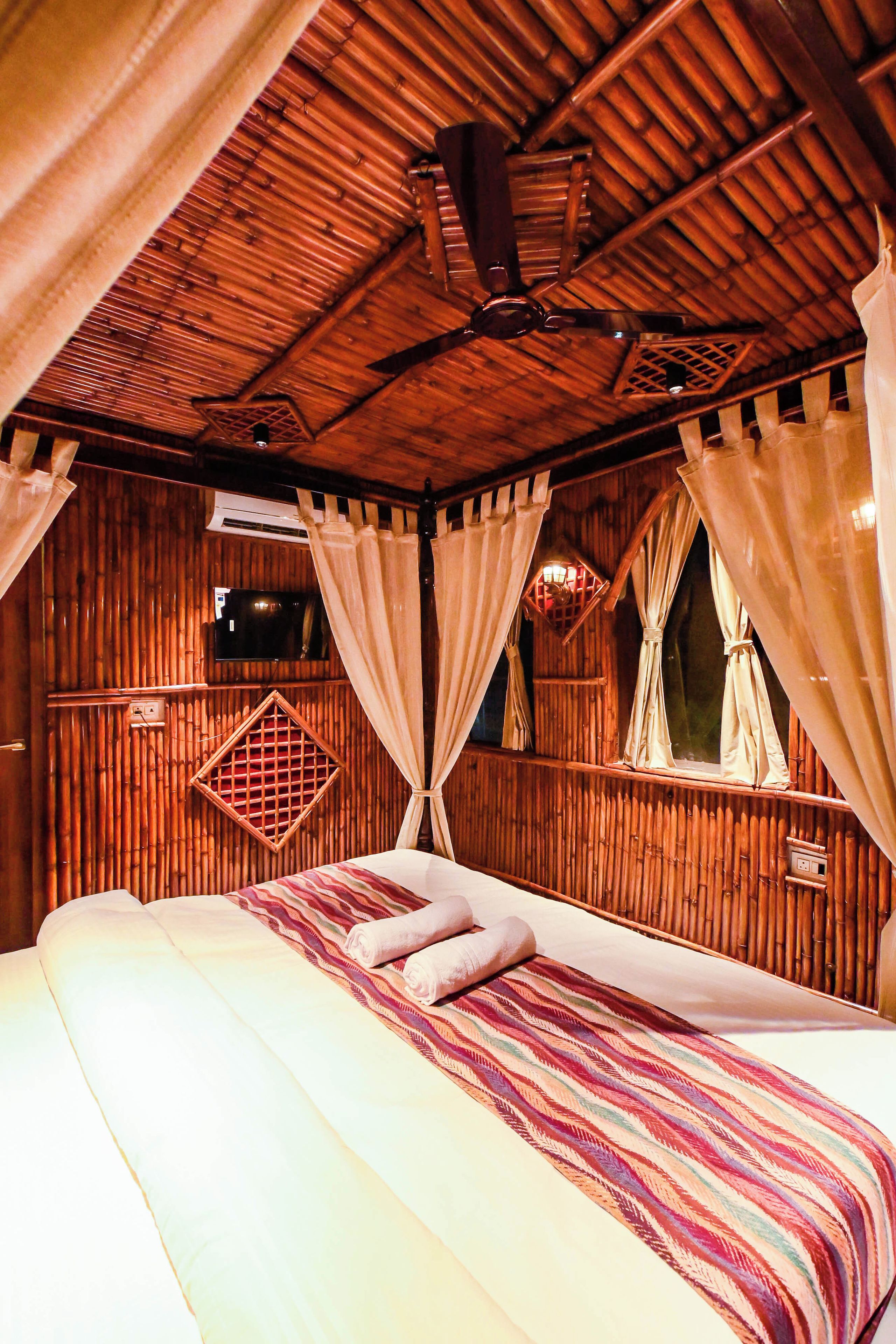 A room with a bed, curtains, a ceiling fan, and a window with a view.