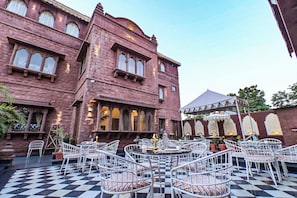 Un patio con mesas al aire libre y un edificio con ventanas arqueadas.