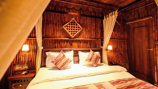 A wooden room with a bed, curtains, and a nightstand. - Inder Fateh Niwas  (Jodhpur)