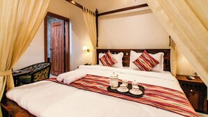 A hotel room with a bed, curtains, a nightstand, a lamp, and a tray with tea set. - Inder Fateh Niwas  (Jodhpur)