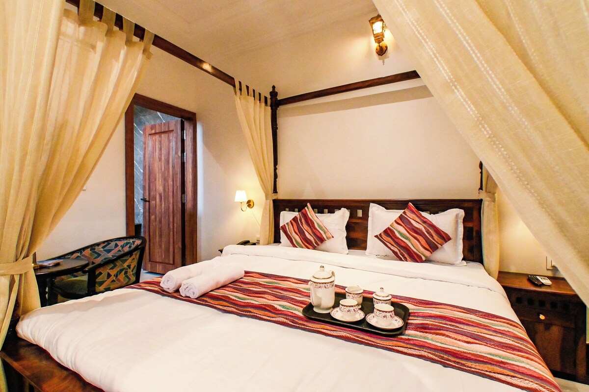 A hotel room with a bed, curtains, a nightstand, a lamp, and a tray with tea set.