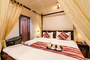 Habitación de hotel con cama, cortinas, mesita de noche, lámpara y bandeja con juego de té.