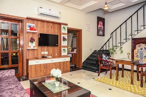 A living room with a wooden cabinet, a flat-screen TV, a staircase, and a dining area with a table and chairs.