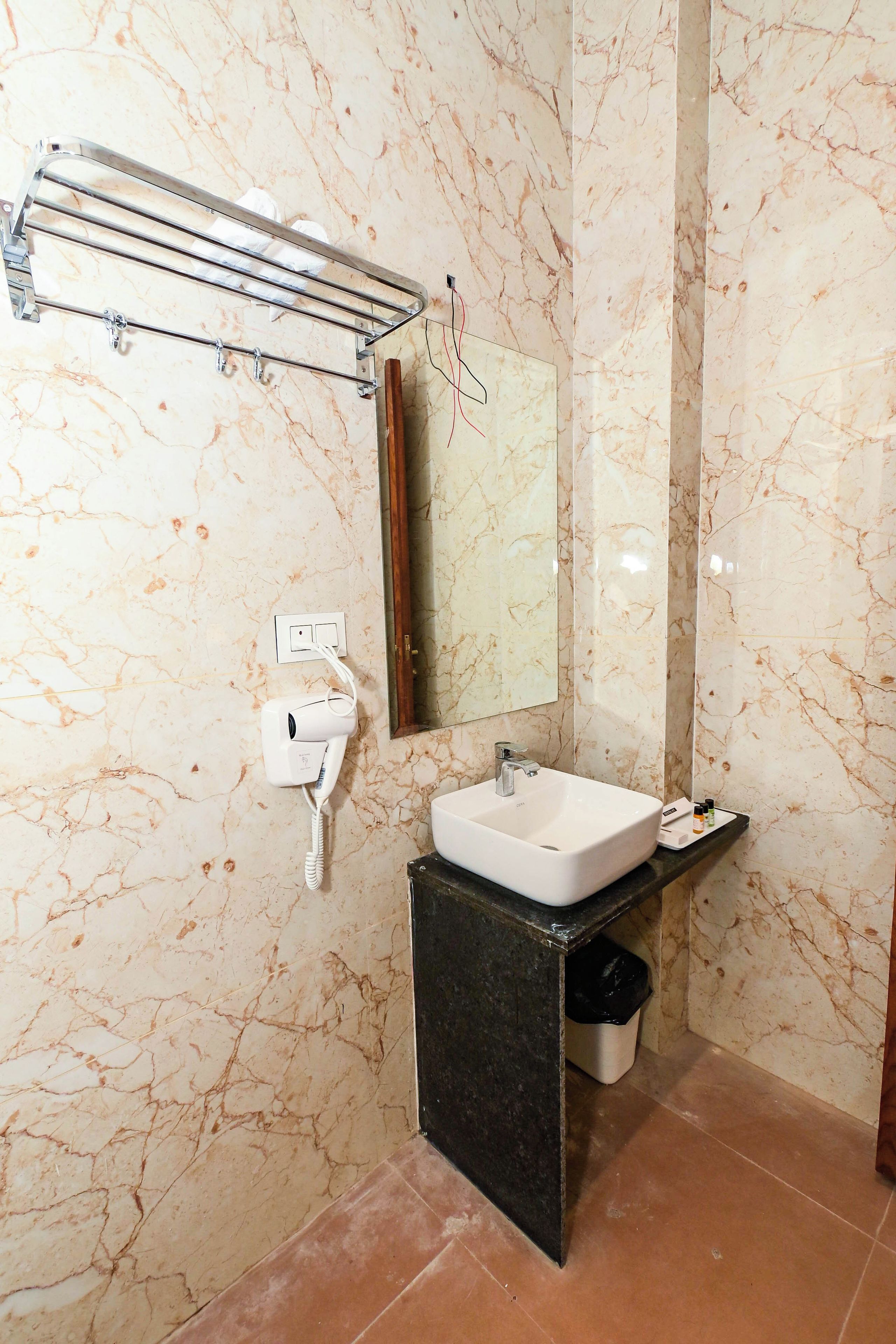 Une salle de bain avec un mur en marbre, un lavabo, un miroir, un porte-serviettes et une poubelle.