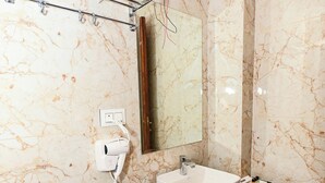 A bathroom with a marble wall, a sink, a mirror, a towel rack, and a trash bin. - Inder Fateh Niwas  (Jodhpur)