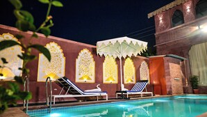 A swimming pool area with lounge chairs and decorative wall panels. - Inder Fateh Niwas  (Jodhpur)