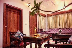 A room with a wooden door, a sofa, a table with books, and a lamp.