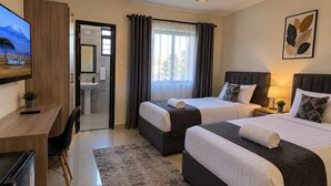 A hotel room with two beds, a desk, a chair, a TV, and a bathroom visible through an open door. - bedsitter r, (Juja)