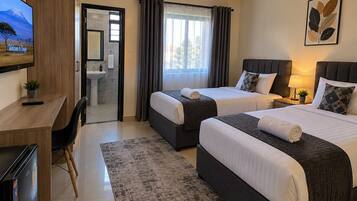 Ein Hotelzimmer mit zwei Betten, einem Schreibtisch, einem Stuhl, einem Fernseher und einem durch eine offene Tür einsehbaren Badezimmer.