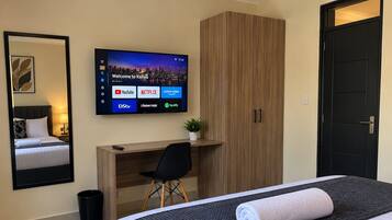 Ein Hotelzimmer mit einem Bett, einem Schreibtisch, einem Fernseher, der Streaming-Dienste anzeigt, einem Kleiderschrank und einer Tür.