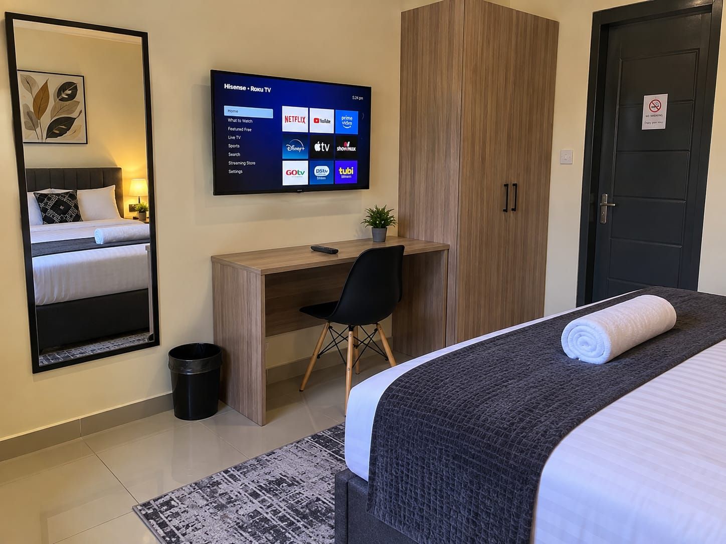 Ein Hotelzimmer mit Bett, Schreibtisch, Sessel, Fernseher mit Streaming-Angeboten, Kleiderschrank und einer Tür mit Rauchverbot-Hinweis.