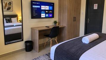 Ein Hotelzimmer mit Bett, Schreibtisch, Sessel, Fernseher mit Streaming-Angeboten, Kleiderschrank und einer Tür mit Rauchverbot-Hinweis.
