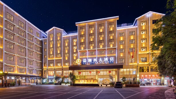 Un hotel de diverses plantes amb cartelleria il·luminada i un aparcament al davant.