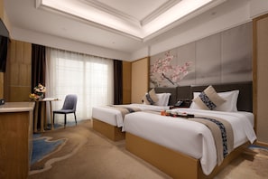 Ein Hotelzimmer mit zwei Betten, einem Schreibtisch, einem Stuhl und einem großen Fenster mit Vorhängen.