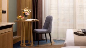 Habitació d'hotel amb escriptori de fusta, una cadira, una taula petita amb un ram de flors i un llit.