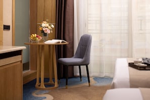 Ein Hotelzimmer mit einem Holztisch, einem Stuhl, einem kleinen Tisch mit Blumen und einem Bett.