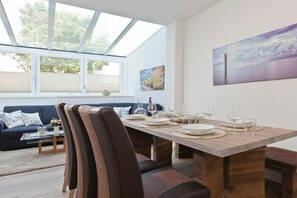 Ein Essbereich mit einem Holztisch, gedeckt für sechs Personen, einer Couch und einem großen Fenster mit Blick auf Bäume.