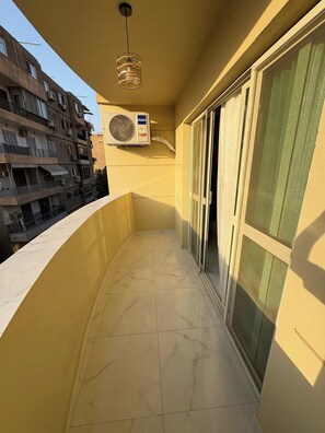 Ein Balkon mit Fliesenboden, Deckenventilator und einem Fenster mit grünem Vorhang.