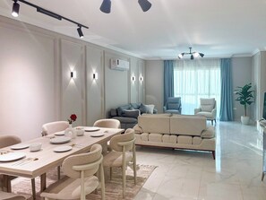 A modern living room with a dining area, featuring a sofa set, a coffee table, and a dining table with chairs. - 3BRs Magnificent City Center Tranquil Apartment (Cairo Governorate)