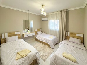 A hotel room with three beds, a large mirror, an air conditioning unit, and a window with curtains. - 3BRs Magnificent City Center Tranquil Apartment (Cairo Governorate)