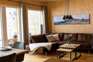 Ein gemütliches Wohnzimmer mit einem braunen Ledersofa, einem Holztisch und einem Gemälde einer Berglandschaft.