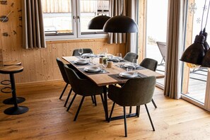 Ein Essbereich mit einem Holztisch, gedeckt für vier Personen, schwarzen Stühlen und Pendelleuchten.