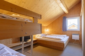 Ein Zimmer mit einem Holzbett, einem Schlafplatz in Etagen, einem Schreibtisch und einem Fenster mit Vorhängen.