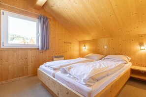 A wooden room with a bed, a window with curtains, and a wall-mounted light. - Cabin with 1 bedroom (St. Georgen am Kreischberg)