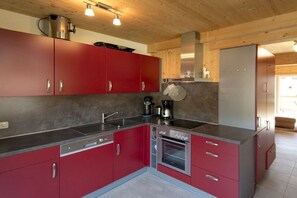 A modern kitchen with red cabinets, stainless steel appliances, and a built-in oven. - Chalet #12b with IR sauna & whirlpool (St. Georgen am Kreischberg)