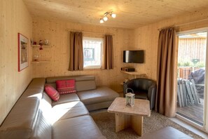 A cozy room with a sofa, a table, a television, and a window with curtains. - Chalet #12b with IR sauna & whirlpool (St. Georgen am Kreischberg)
