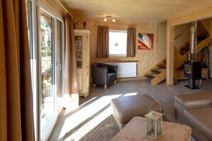 Un intérieur chaleureux avec une cheminée, un escalier et une vue dégagée sur l’extérieur grâce à de grandes fenêtres.