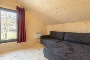 A room with a wooden ceiling, a grey sofa, a window with red curtains, and a wall-mounted heater. - Cabin with 1 bedroom (St. Georgen am Kreischberg)
