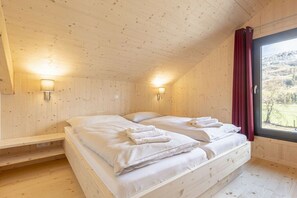 Une chambre de style cabane en bois, avec deux lits, une fenêtre avec des rideaux et des lampes fixées au mur.