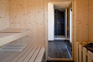 Una sauna in legno con una panca, un angolo doccia con porta in vetro e pavimento piastrellato.