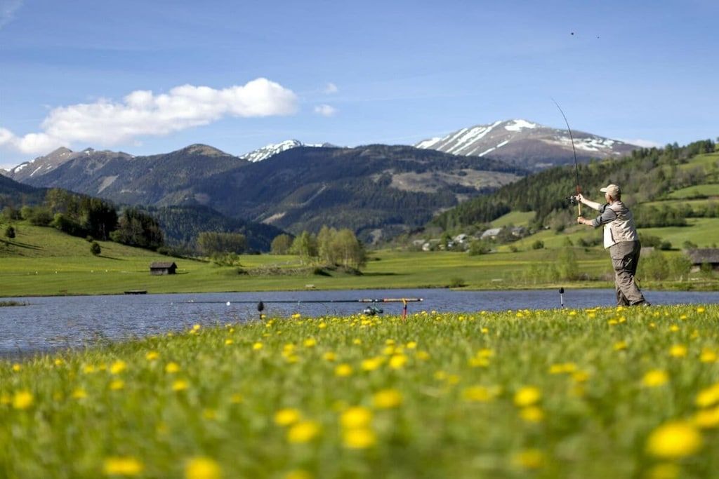 A person fishing by a lake with mountains in the background.
