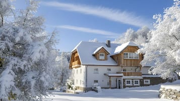 Une grande maison en bois, dont le toit est recouvert de neige, entourée d’arbres chargés de neige.
