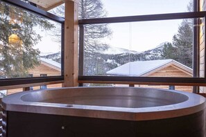 A spa area with a large bathtub, wooden walls, and a view of snow-covered mountains. - Cabin in Turrach with sauna and terrace (Turrach)