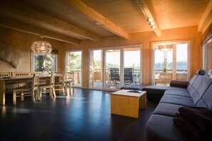 Un interior moderno con zona de comedor de madera, un sofá y un amplio ventanal corredera que da a un espacio exterior.