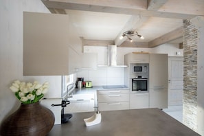 A modern kitchen with white cabinetry, a stone accent wall, and a vase of white flowers on the counter. - Cabin in Turrach with sauna and balcony (Turrach)