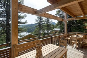 Eine Holzdielen-Terrasse mit Tischen und Stühlen mit Blick auf eine bewaldete Berglandschaft.