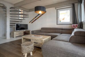 A modern living room with a sectional sofa, a wooden coffee table, a television on a wooden stand, and a unique hanging light fixture. - Cabin in Turrach with sauna and balcony (Turrach)