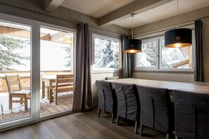 Ein modernes Interieur mit einem Holzespeisetisch und Stühlen, großen Fenstern mit Vorhängen sowie Pendelleuchten.