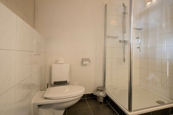 Uma casa de banho moderna com sanita, chuveiro com parede de vidro e um lixo.