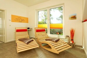 Ein Zimmer mit zwei Holzliegen, einem Fenster mit Blick auf Grünflächen und einem Wandzeichen.