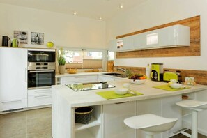 A modern kitchen with white cabinetry, a central island with stools, a built-in oven, and a wooden accent wall. - Str. d. Freundschaft 30c (Karlshagen)