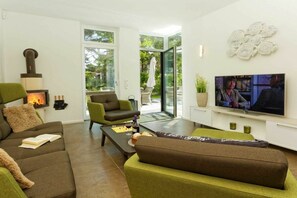A modern living room with a fireplace, comfortable seating, a television, and a glass door leading to an outdoor area. - Str. d. Freundschaft 30c (Karlshagen)
