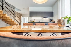 A modern kitchen with a central island, a staircase, and a dining area with a glass table. - Holiday home with 1 bedroom (Fuhlendorf)