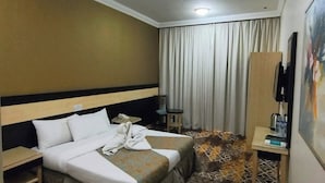 Habitación de hotel con cama, escritorio, silla, televisión y un cuadro en la pared.