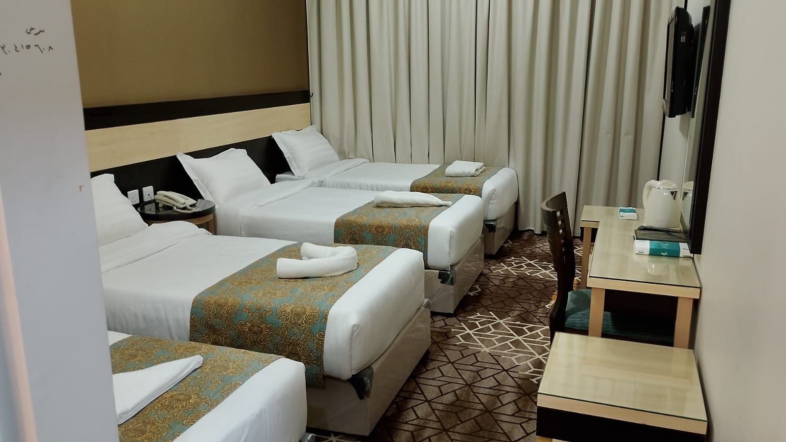 Habitación de hotel con tres camas, un escritorio y un espejo.