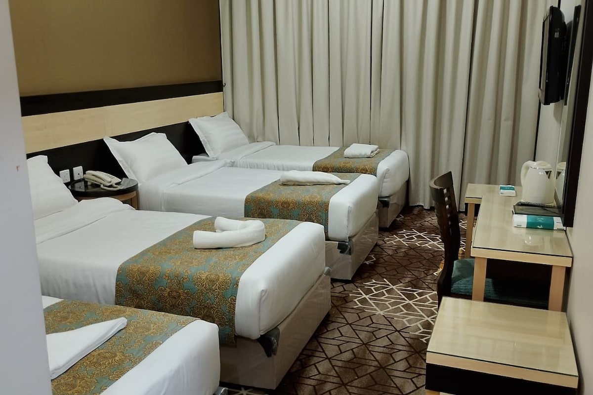 Ein Hotelzimmer mit drei Betten, einem Schreibtisch und einem Spiegel.